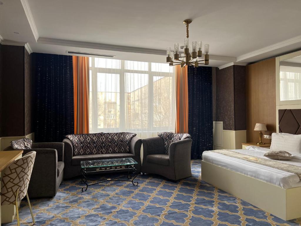 a bedroom with a bed and a couch and chairs at Almaty Grand Erbil Hotel in Almaty