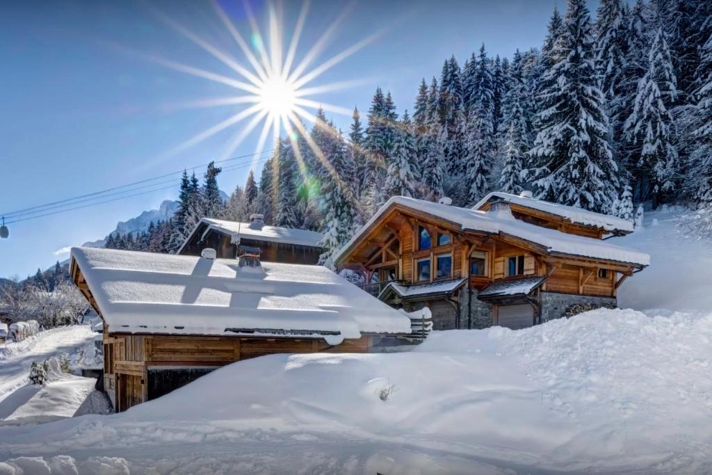 a log cabin in the snow with the sun behind it at Chalet Timan - OVO Network in La Clusaz
