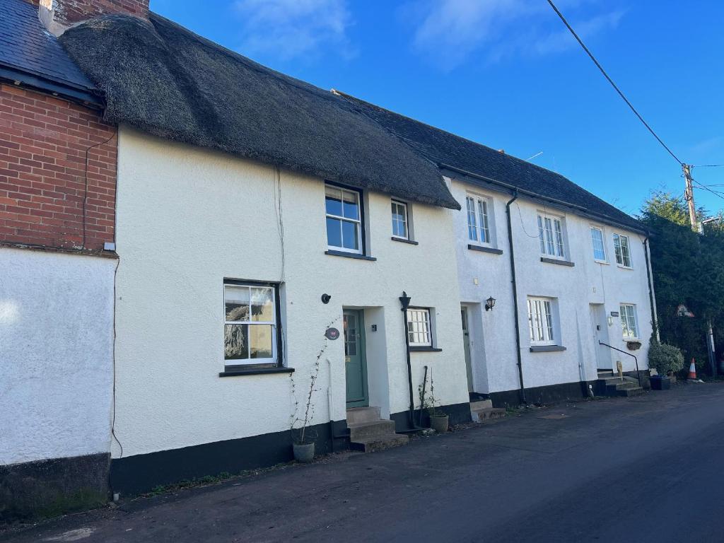 ein weißes Haus mit einem Strohdach auf einer Straße in der Unterkunft Jean's Cottage in Exeter