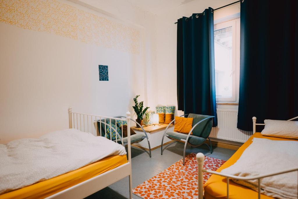 a bedroom with two beds and a chair and a window at Hostel Très Schick in Bamberg