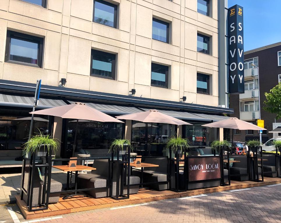 um restaurante com mesas e guarda-sóis em frente a um edifício em Savoy Hotel Rotterdam em Roterdão