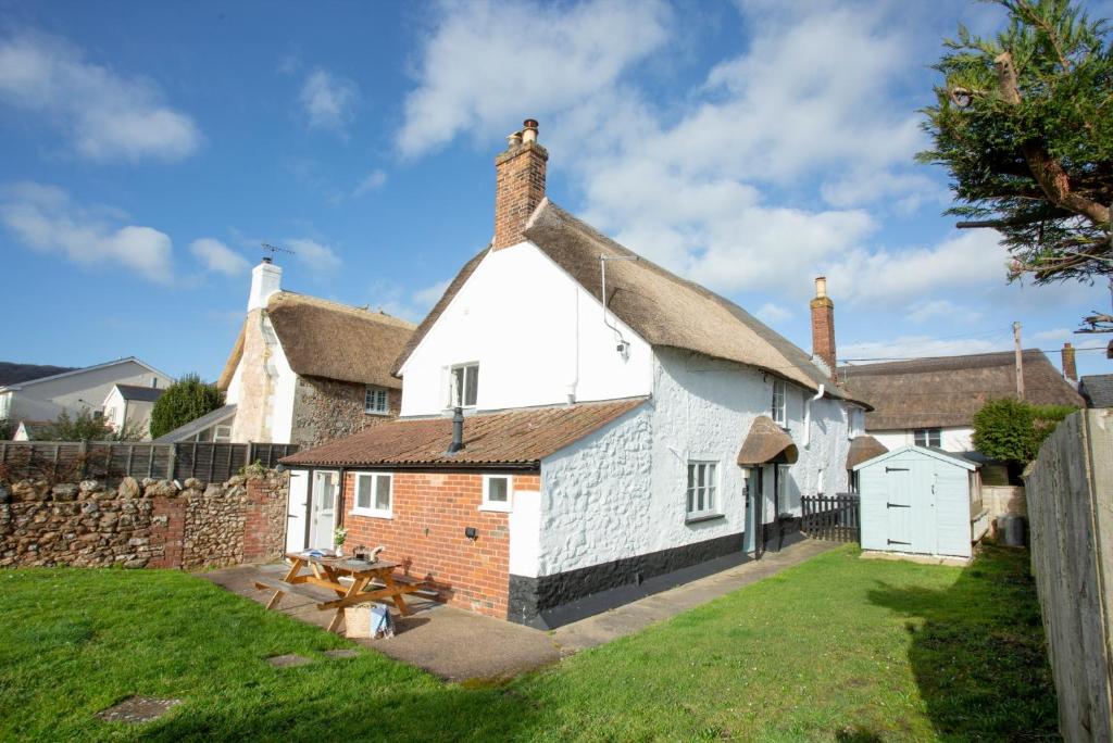 a white cottage with a thatched roof with a picnic table at Fox Cottage in Sidbury