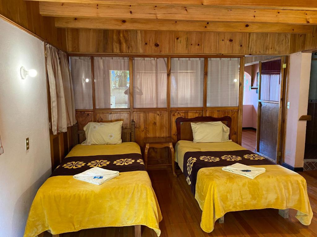 two beds in a room with wooden walls at Posada Quetzalin in Cuetzalán del Progreso