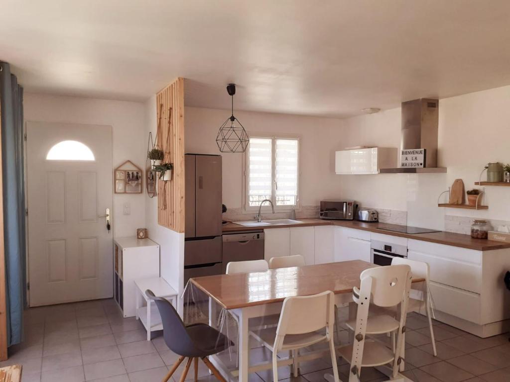 eine Küche mit einem Holztisch und weißen Stühlen in der Unterkunft Maison ensoleillée de plain-pied ouvert sur un jardin clôturé in Mallemoisson