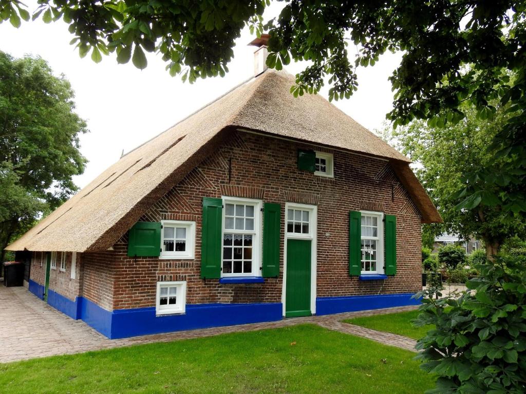 un bâtiment avec un toit de chaume et des fenêtres vertes dans l'établissement Farmhouse in Staphorst with sauna, à Rouveen