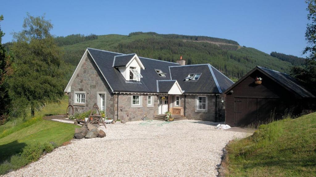 a large stone house with a garage and a hill at The Byre in Strathyre