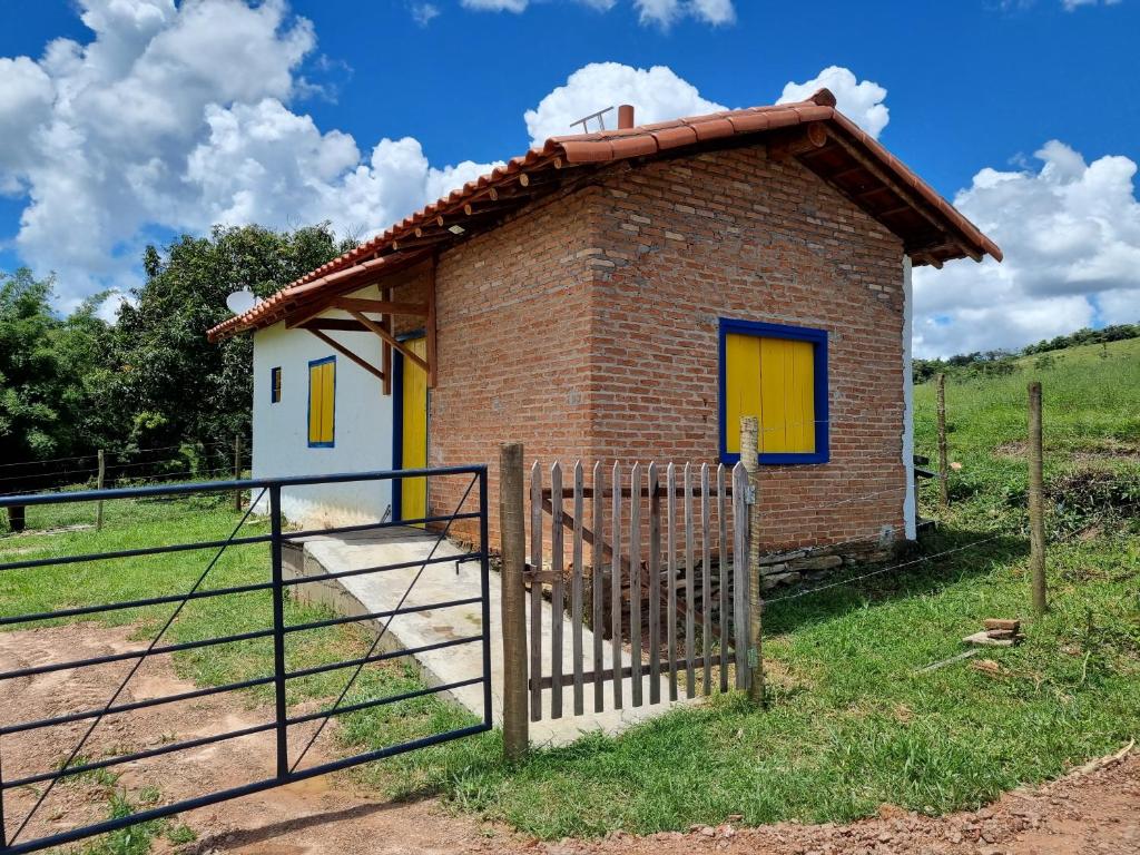 una pequeña casa de ladrillo con puertas amarillas y una valla en Chalé Boa Vista en Carrancas