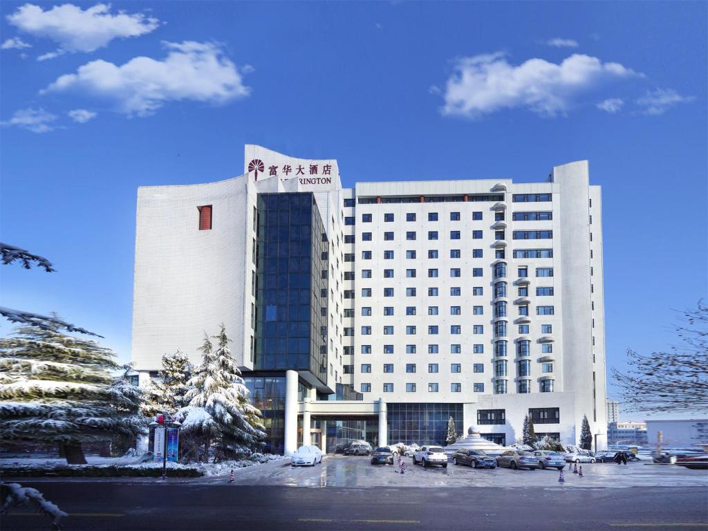 ein großes weißes Gebäude mit auf einem Parkplatz geparkten Autos in der Unterkunft 潍坊富华大酒店B座 The Farrington Hotel B in Weifang