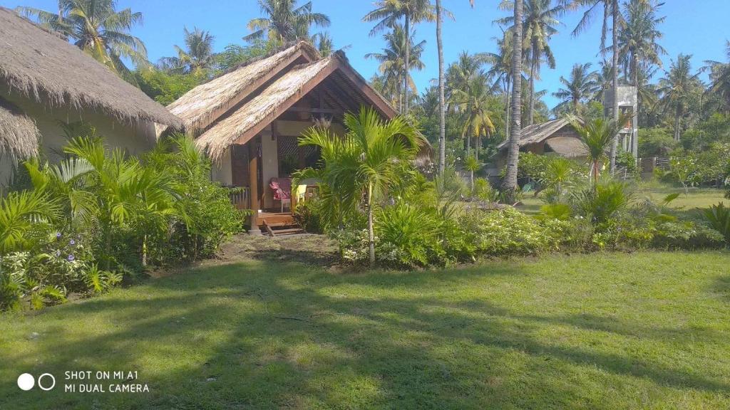 a house with a grass roof and a yard at Rumah Sunyi in Gili Trawangan