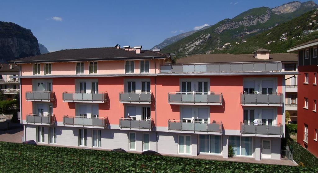 a red building with balconies and mountains in the background at Hotel Garnì Corallo in Nago-Torbole