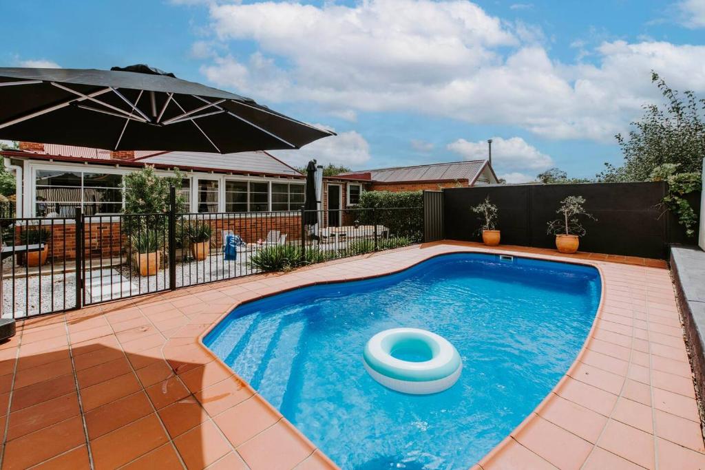 a swimming pool with an umbrella next to a house at Mortimer Cottage - A Pool Oasis in Heart of Mudgee in Mudgee