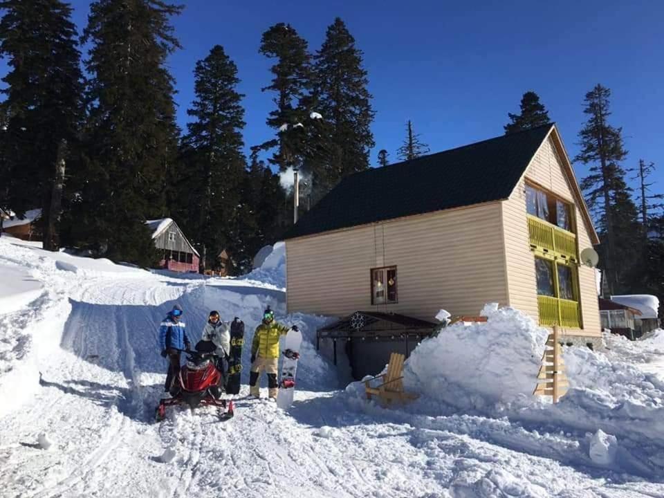 a group of people standing in the snow near a cabin at კოტეჯი ბახმაროში WoodenHouse Sunrise in Bakhmaro