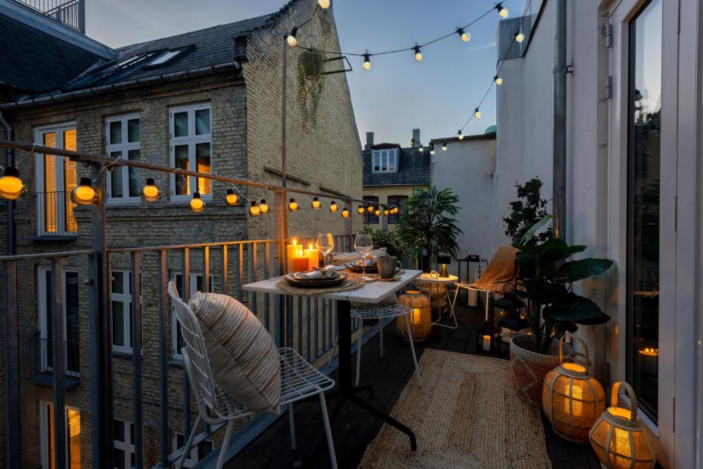 d'un balcon avec une table, des chaises et des lumières. dans l'établissement Sanders Leaves - Chic Three-Bedroom Apartment In Downtown Copenhagen, à Copenhague