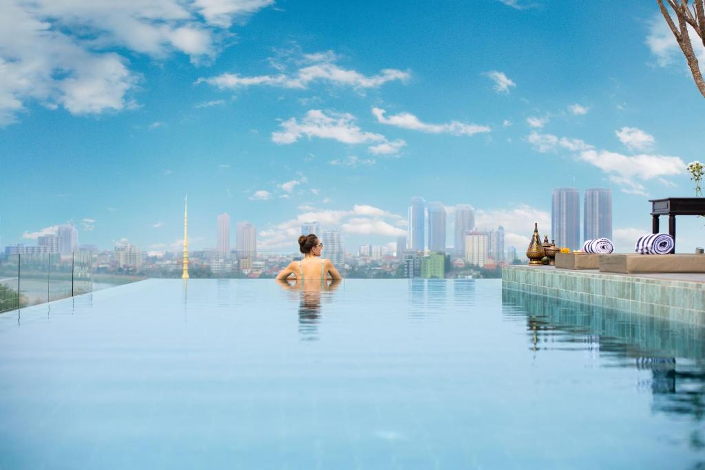 a man in a infinity pool with a city in the background at GLOW PARK HOTEL Grand Royal Palace in Phnom Penh