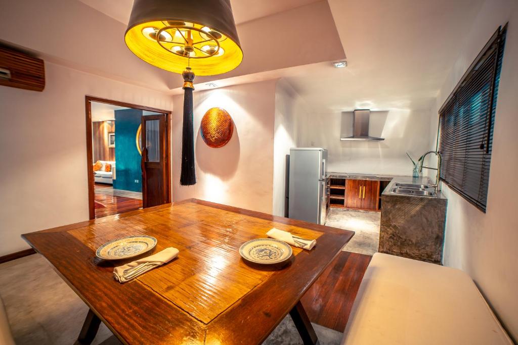 A wood dining table set for two beside a compact kitchenette and adjoining room.