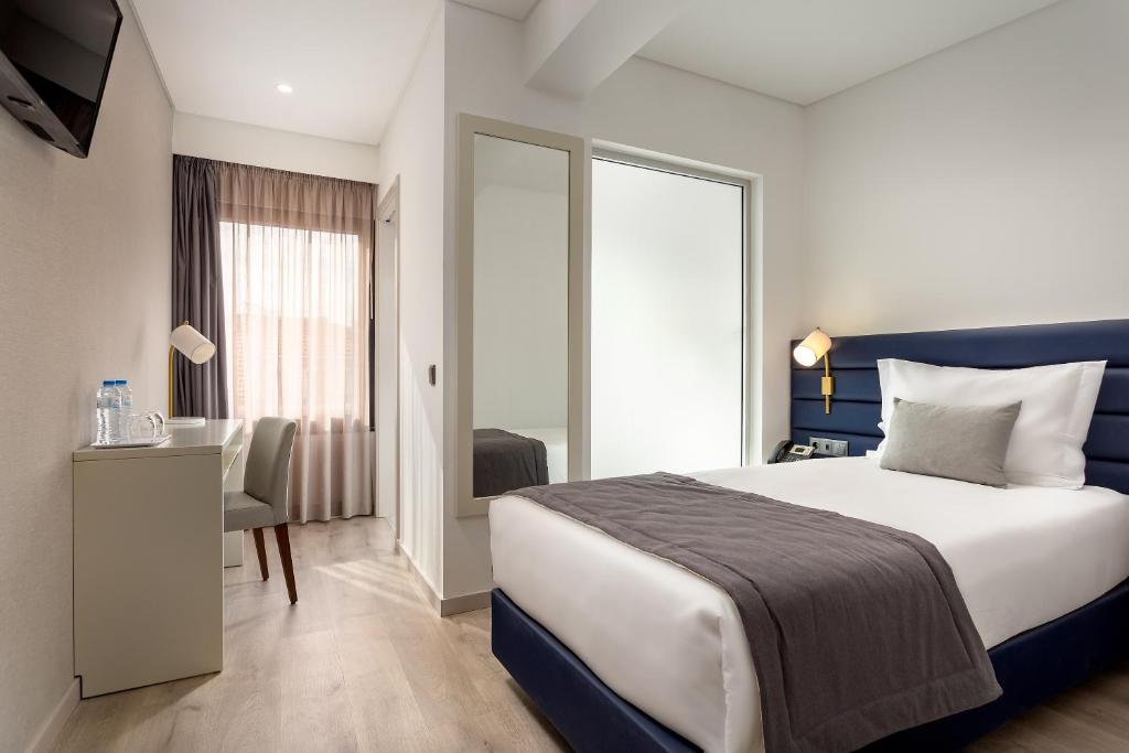 a hotel room with a bed and a desk and a window at Empire Marquês Hotel in Lisbon