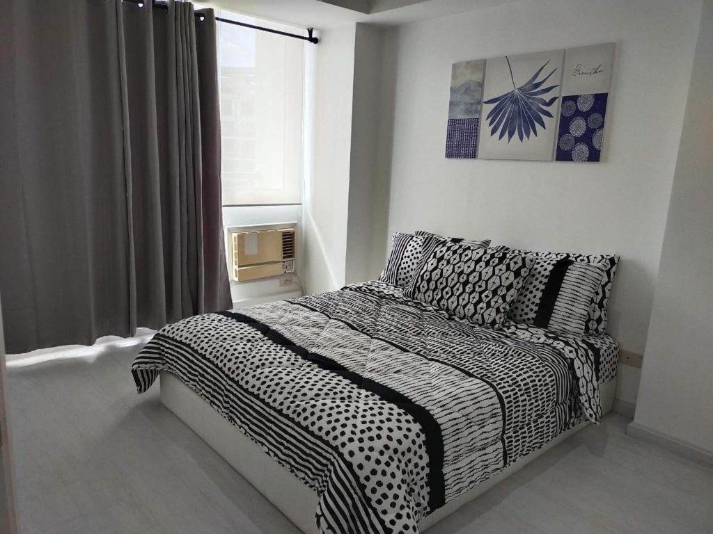 um quarto com uma cama com lençóis brancos e pretos e uma janela em Staycation at Azure by Melissa em Manila