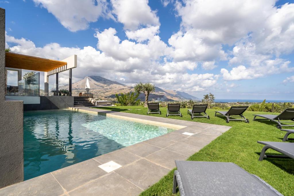 uma piscina com cadeiras e montanhas ao fundo em Villa vista mare Piscina e SPA em Castellammare del Golfo