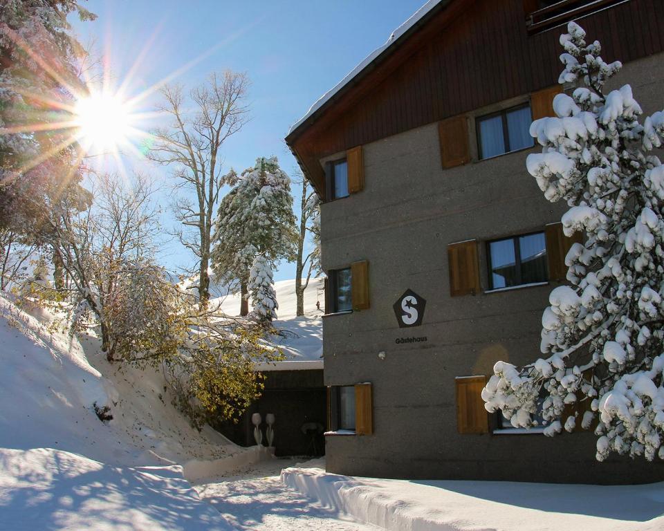 um edifício na neve com o sol atrás dele em Gästehaus by Stoos Hotels em Stoos
