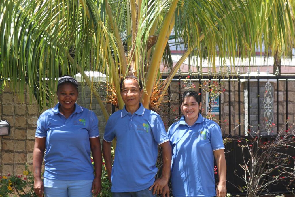 tres personas en camisas azules de pie junto a una palmera en Chez Augustine, en Baie Lazare Mahé