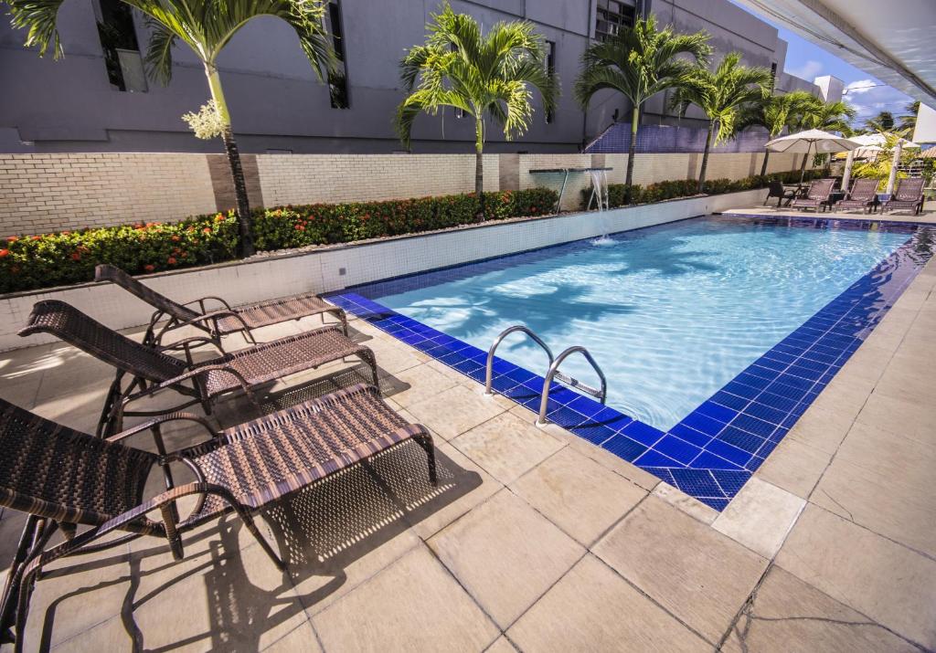 una piscina con bancos y palmeras en un hotel en IMPERIAL TAMBAU Flat by PenareiaTurBr, en João Pessoa