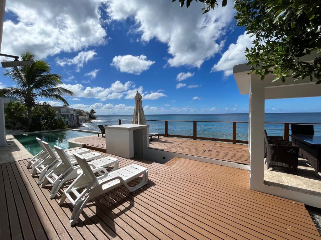 a deck with chairs and a pool and the ocean at Sunset Surf Villa Beacon Hill in Simpson Bay