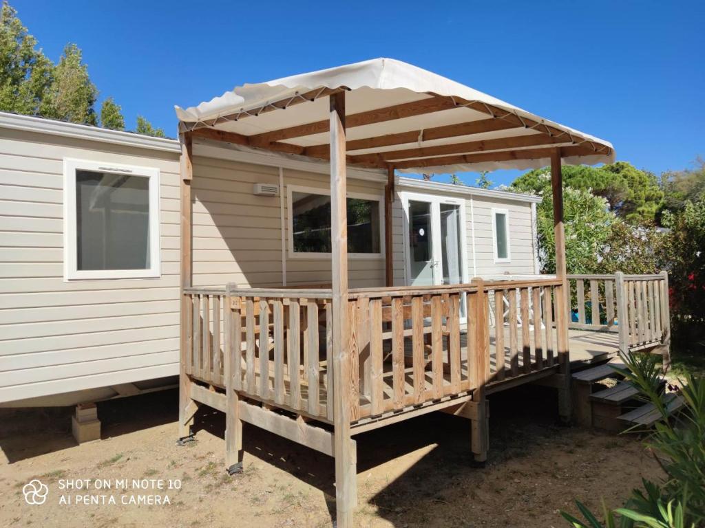a tiny house with a porch and an umbrella at Location Mobilhome in Narbonne-Plage