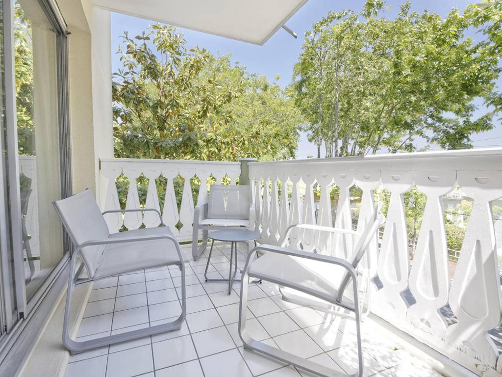 une terrasse couverte avec des chaises blanches et une balustrade blanche dans l'établissement Appartement T2 à Arcachon, proche plage, avec balcon, rénové, dans quartier calme et verdoyant - FR-1-433-79, à Arcachon