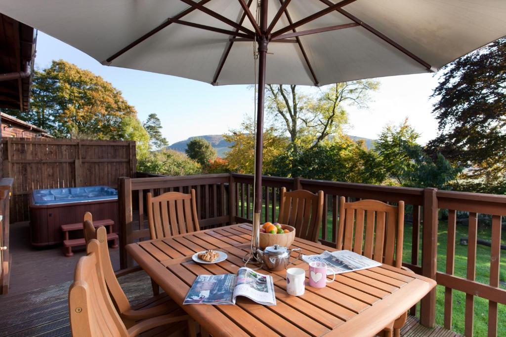 a wooden table with an umbrella on a deck at Copper Beech Lodge with Hot Tub in Cupar