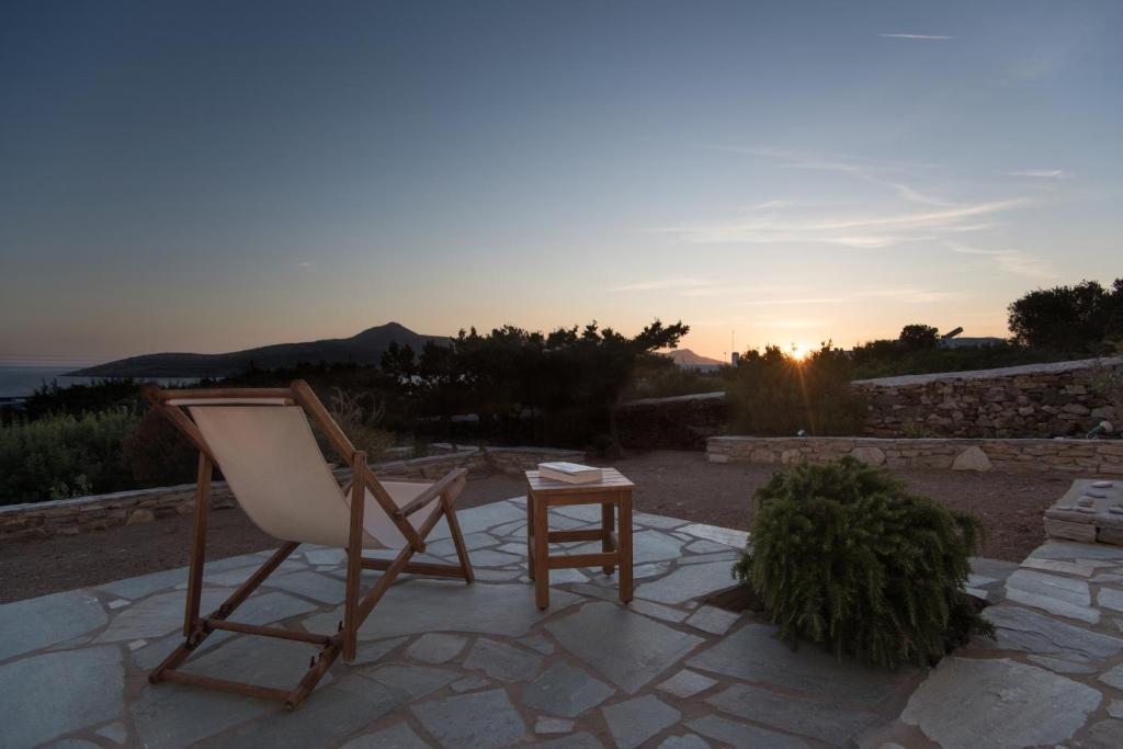 a chair and a table on a patio with the sunset at Oliaros seaside complex in Agios Georgios