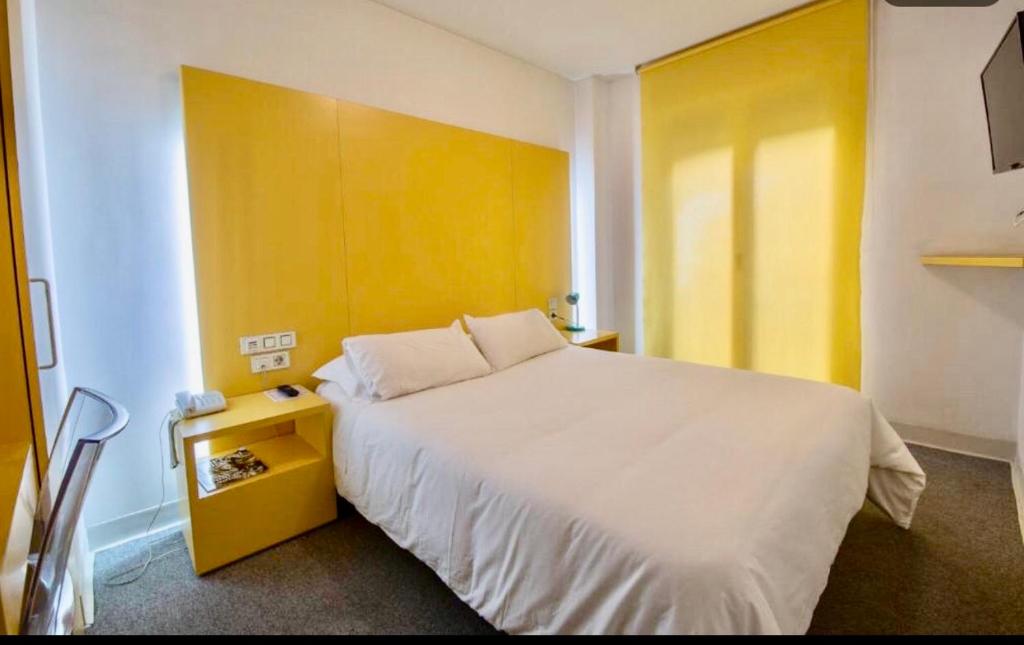 a bedroom with a white bed and a yellow wall at Hostal Albany in León