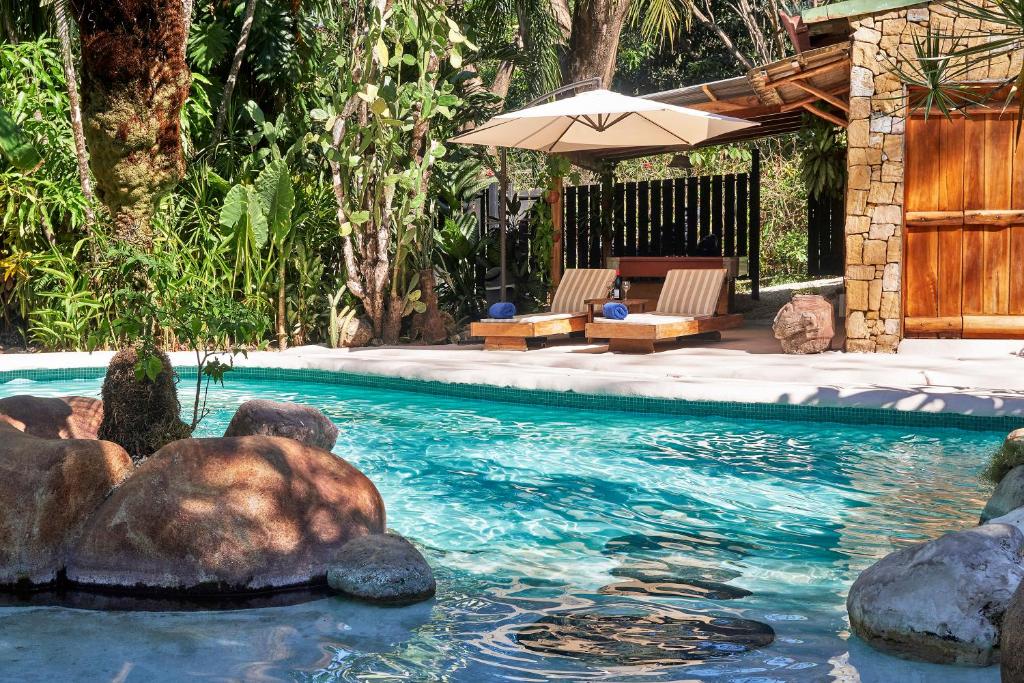a swimming pool with two chairs and an umbrella at Havana Lodge in Mal País