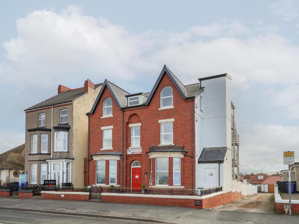 a red brick house with a red door on a street at Ty Canol in Rhyl