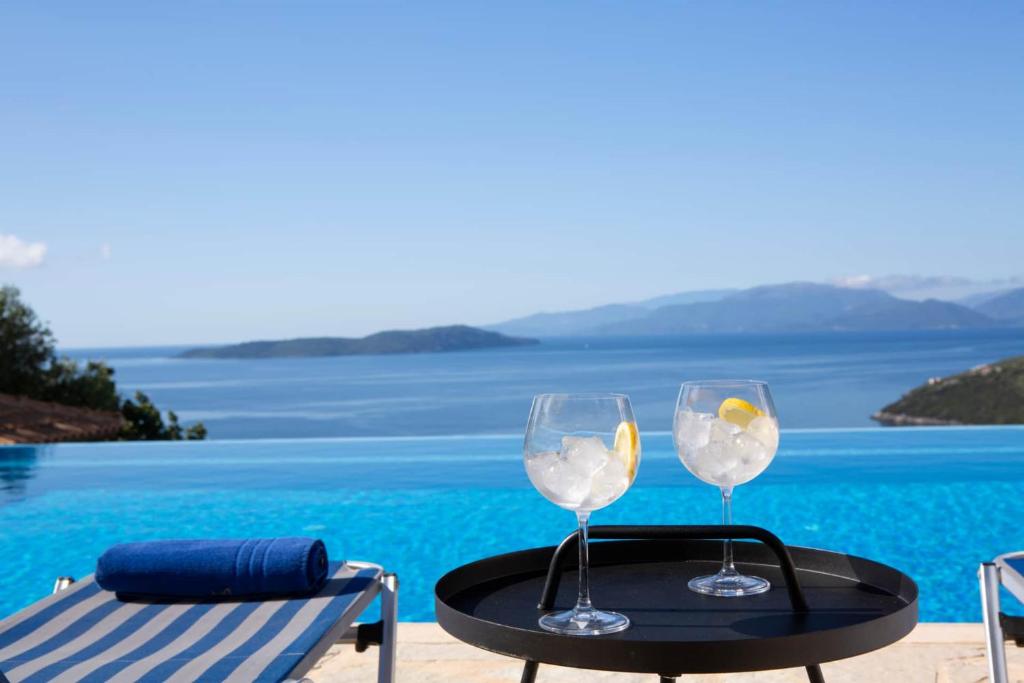 two wine glasses on a table next to a pool at Villa Thaleia in Sivota