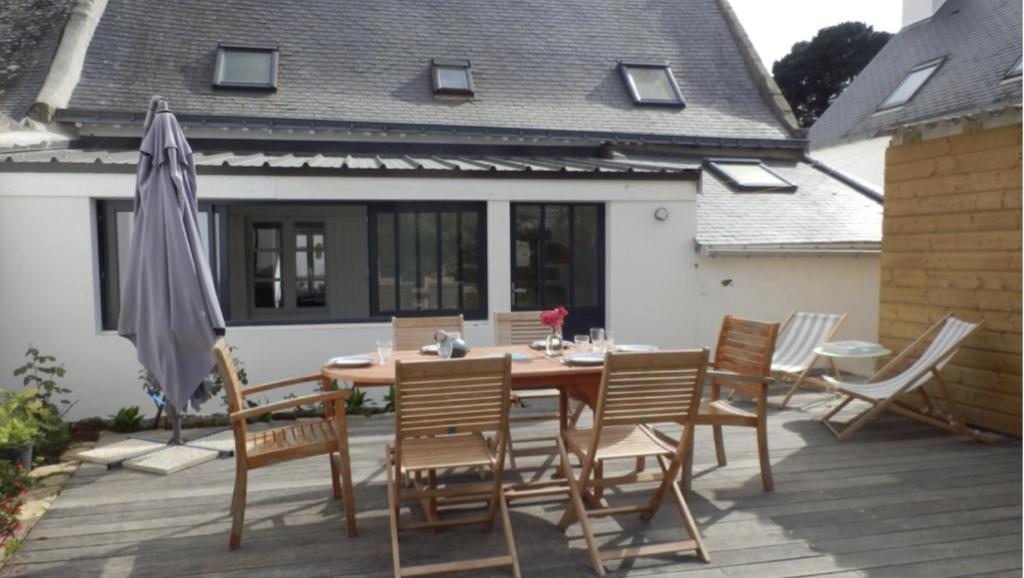 einen Holztisch mit Stühlen und einem Sonnenschirm auf einer Terrasse in der Unterkunft Maison bord de mer ・La côtière・ in Piriac-sur-Mer