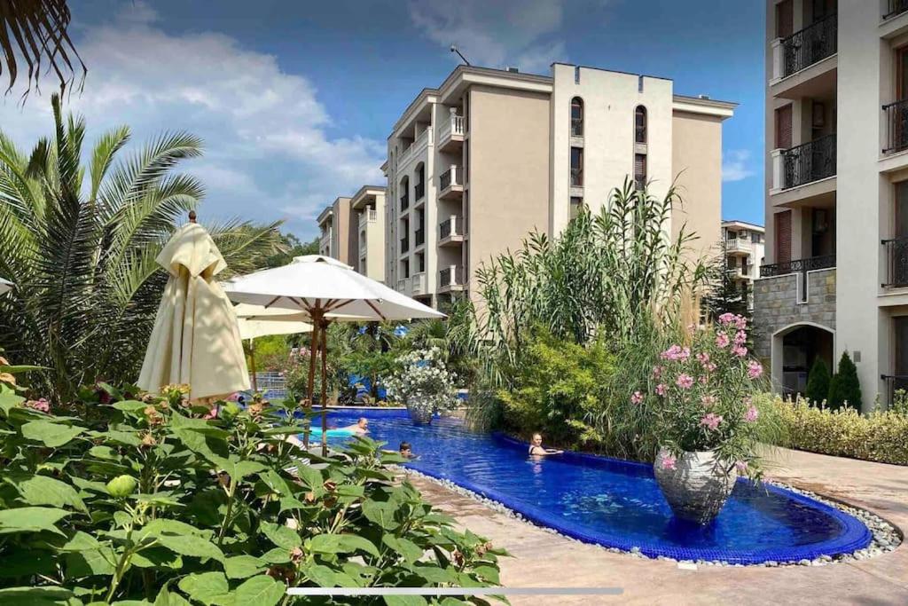 a swimming pool with an umbrella and some buildings at Deluxe Appartement in Cascadas Resort Sunny Beach in Sunny Beach