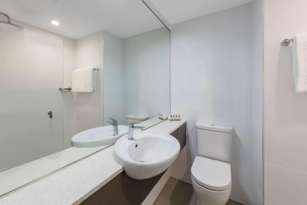 a white bathroom with a sink and a toilet at Travelodge Hotel Sydney Airport in Sydney
