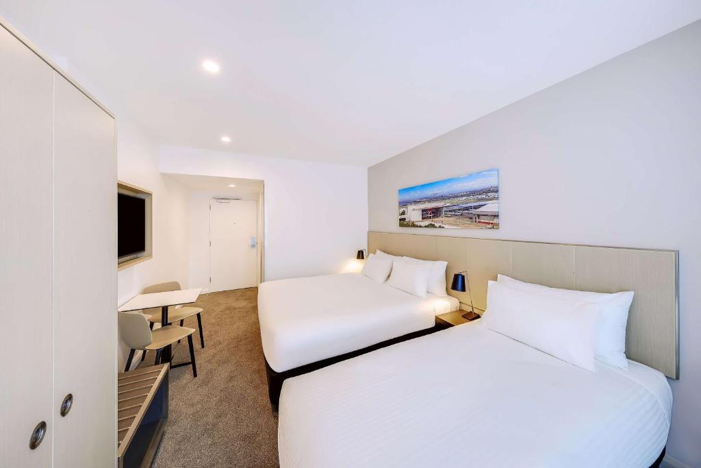 a hotel room with two beds and a desk at Travelodge Hotel Sydney Airport in Sydney