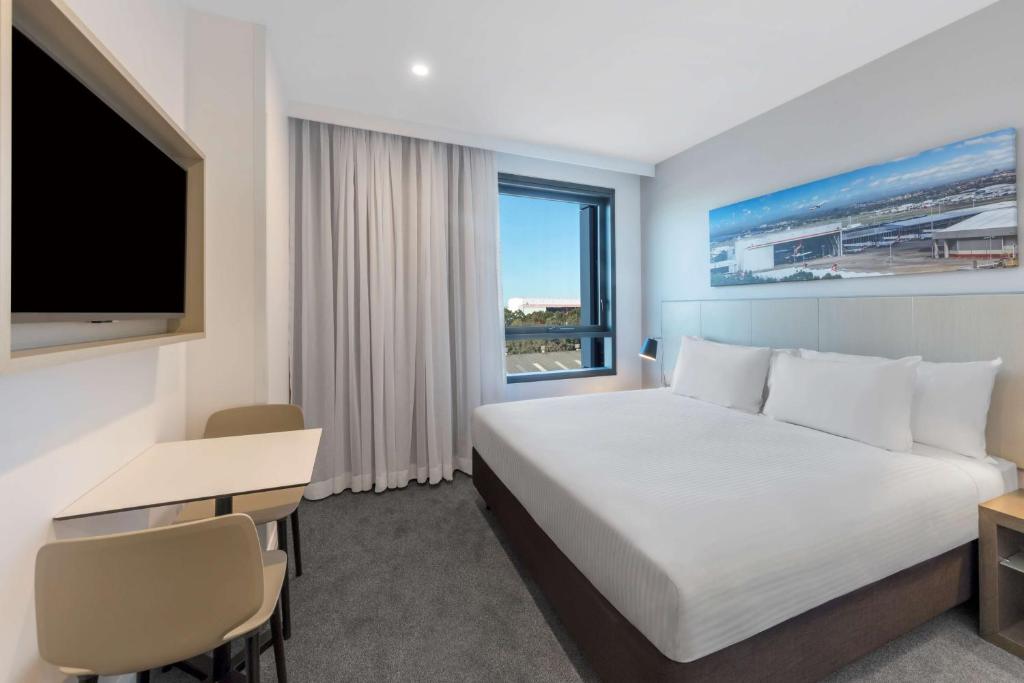 a hotel room with a bed and a desk and a television at Travelodge Hotel Sydney Airport in Sydney