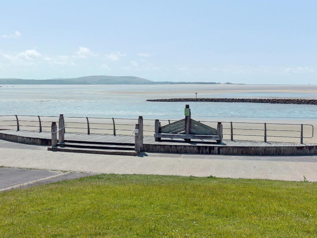 eine Bank auf einem Gehweg neben einem Wasserkörper in der Unterkunft Beachlands in Llanelli