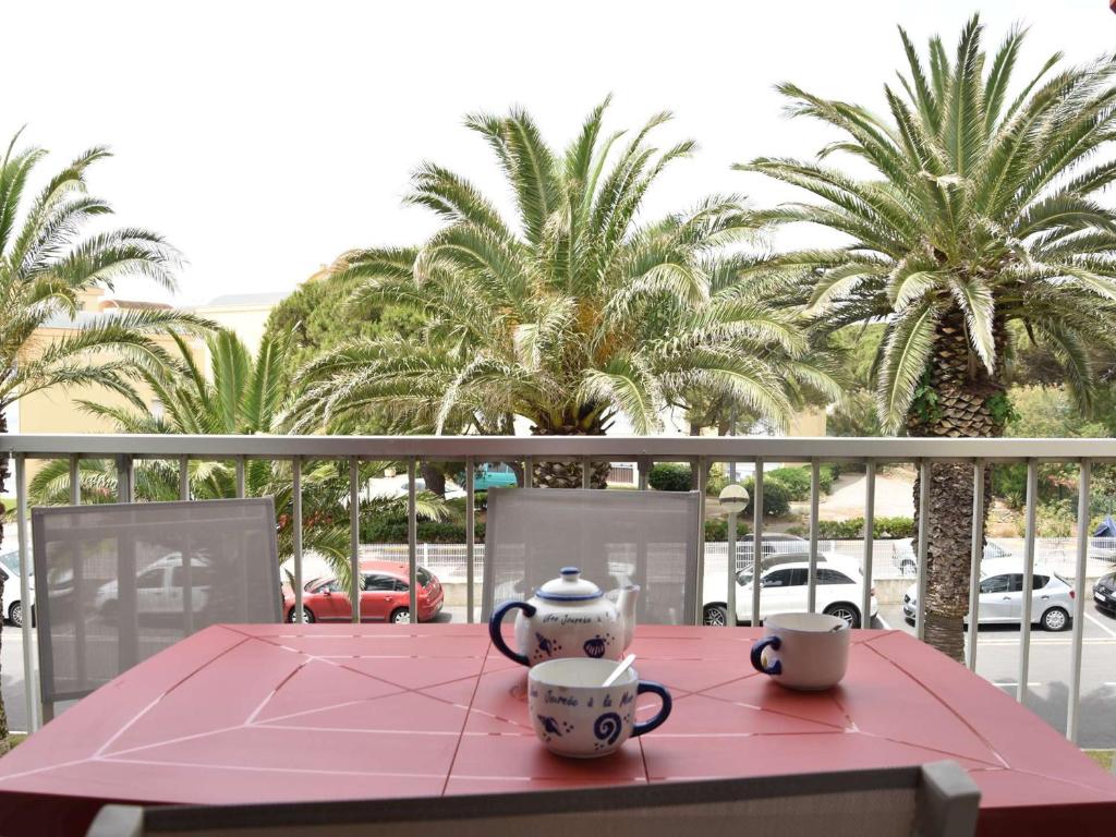 deux tasses sur une table rose sur un balcon avec des palmiers dans l'établissement Appartement 2 pièces avec climatisation, proche plage - Gruissan - FR-1-229-788, à Gruissan