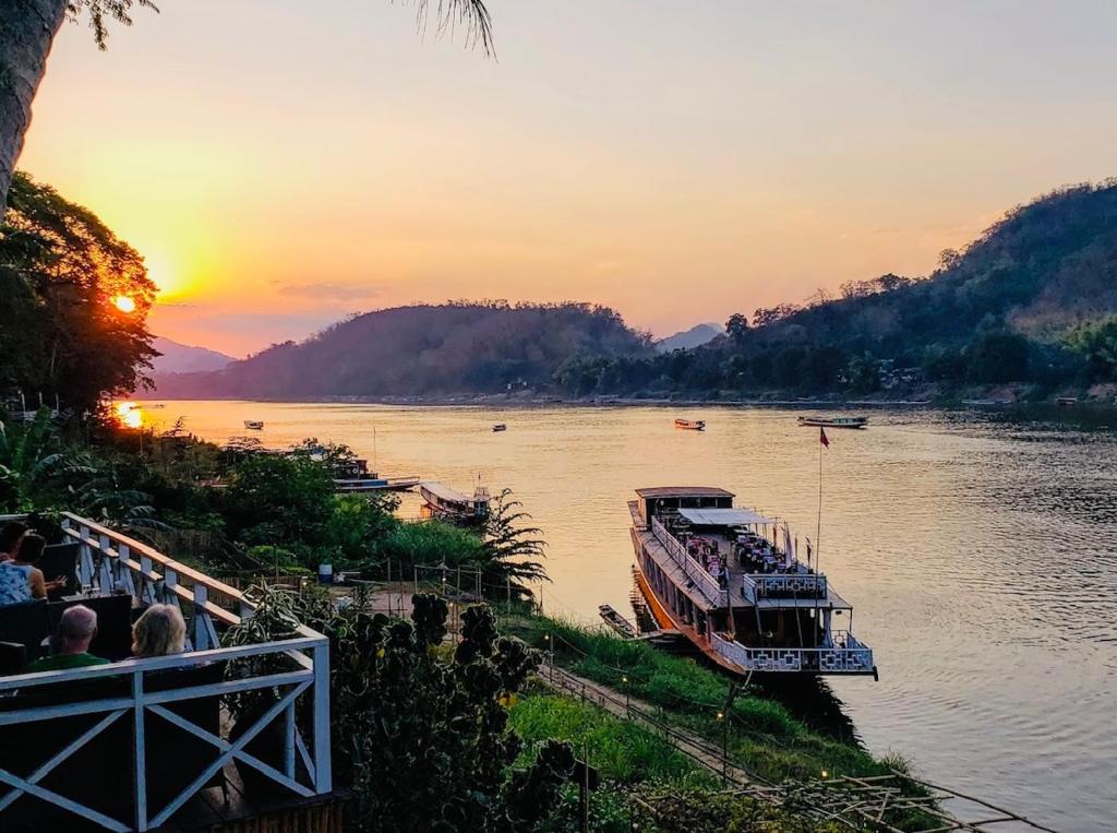 琅勃拉邦的住宿－Villa Alounsavath Mekong Riverside，日落时分沿着河流航行的船只