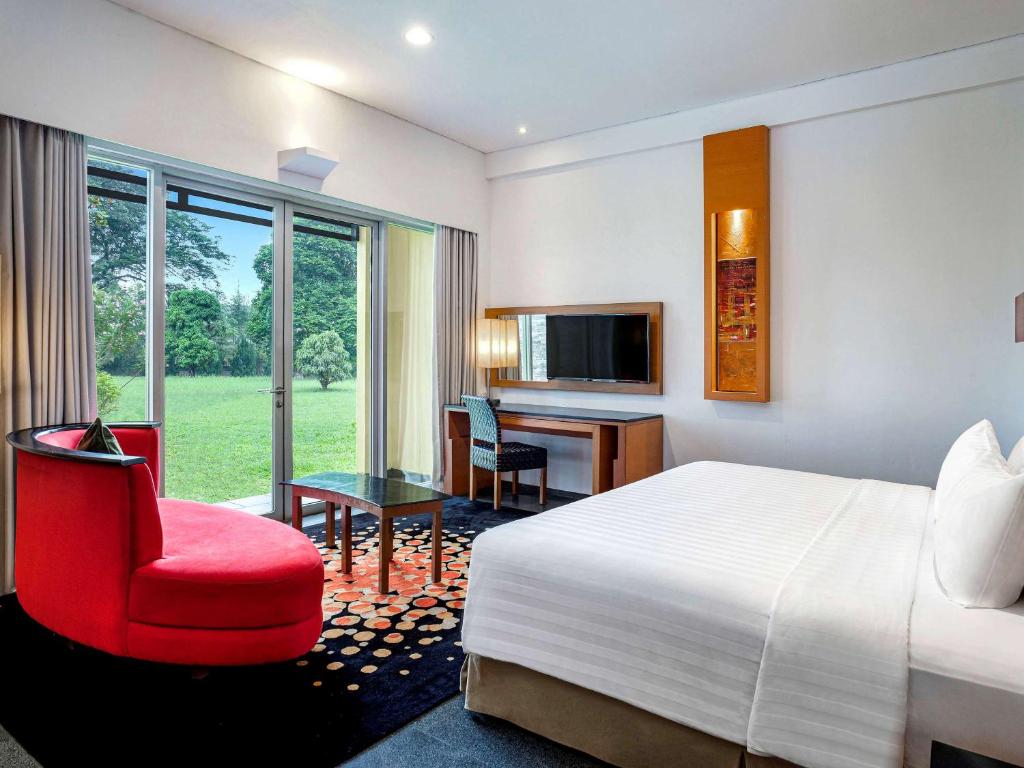 Habitación de hotel con cama, silla roja y escritorio. en Novotel Palembang en Palembang