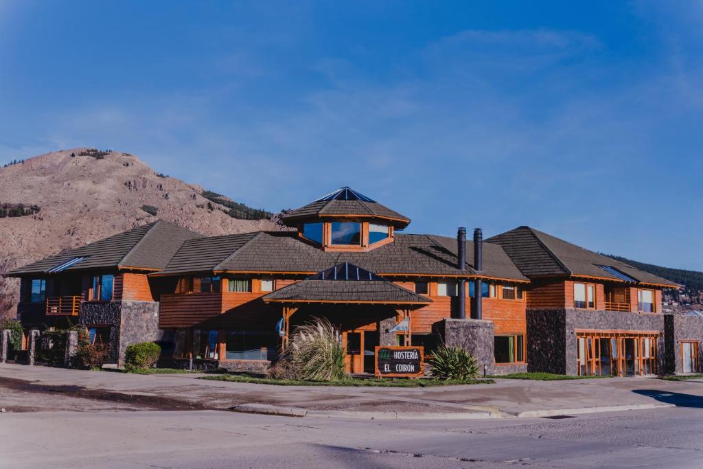 ein großes Holzhaus mit einem Berg im Hintergrund in der Unterkunft Hostería El Coirón in Esquel