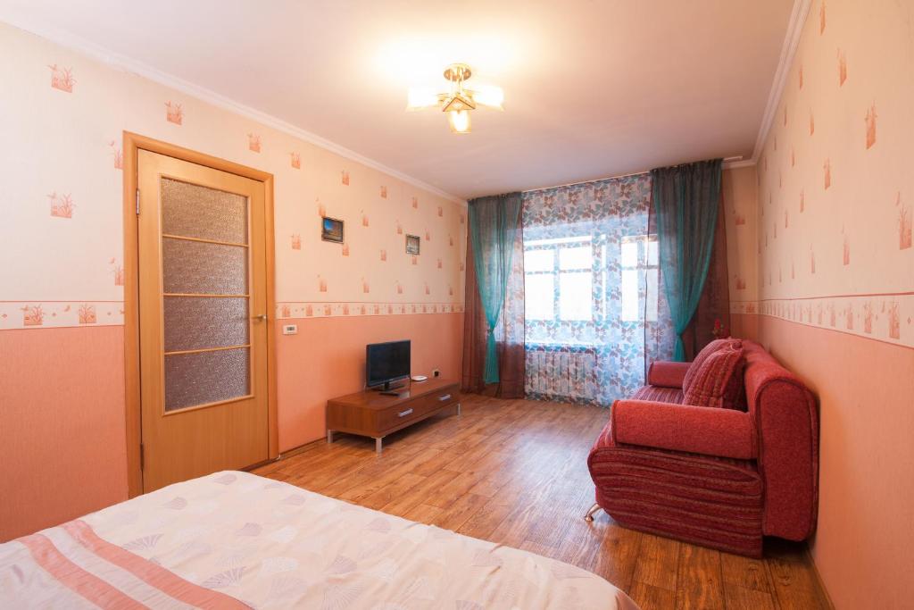 a bedroom with a bed and a chair and a television at Kvartirov Apartment at Surikova in Krasnoyarsk