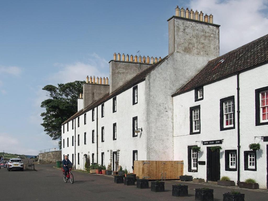 a man riding a bike in front of a white building at Cobble Cottage in Cramond