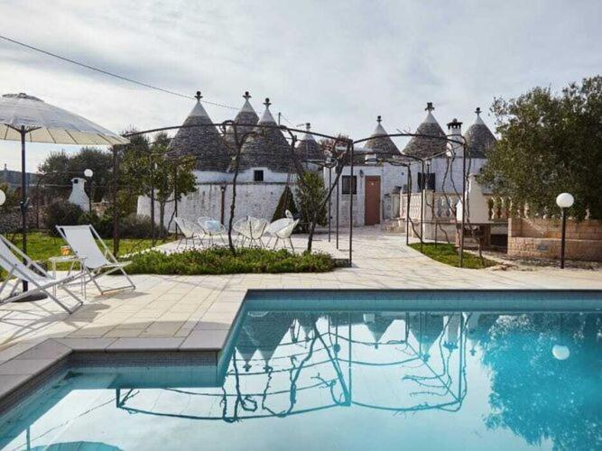 einen Pool mit Stühlen und Sonnenschirmen neben einem Haus in der Unterkunft Holiday rental Trulli Azzalema,Cisternino in Cisternino