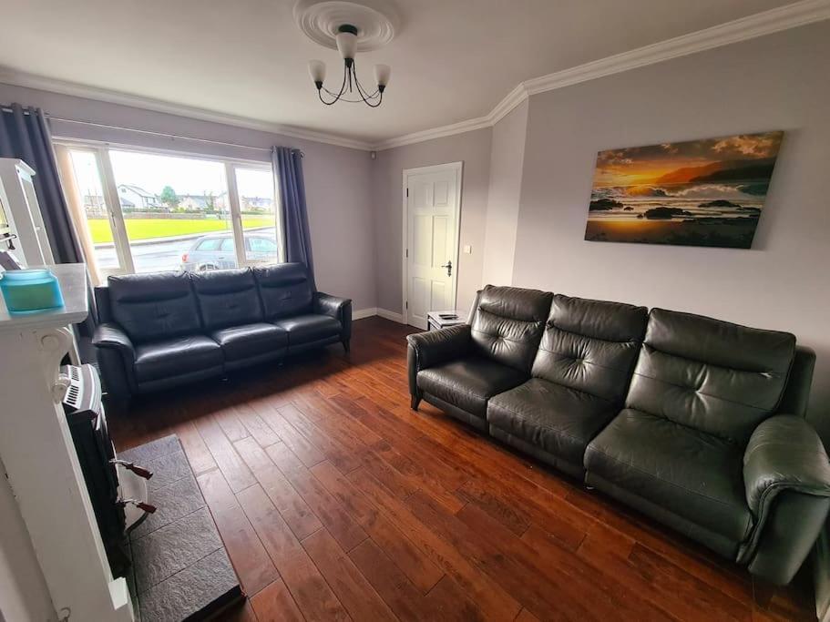 a living room with black leather furniture and a window at Bundoran Seaside Stays House - WiFi, large spacious home in Bundoran