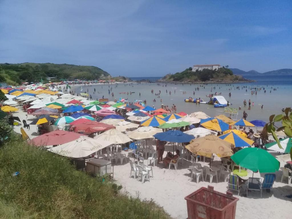 un groupe de personnes assises sur une plage avec des parasols dans l'établissement Casa temporada paraíso, à Cabo Frio