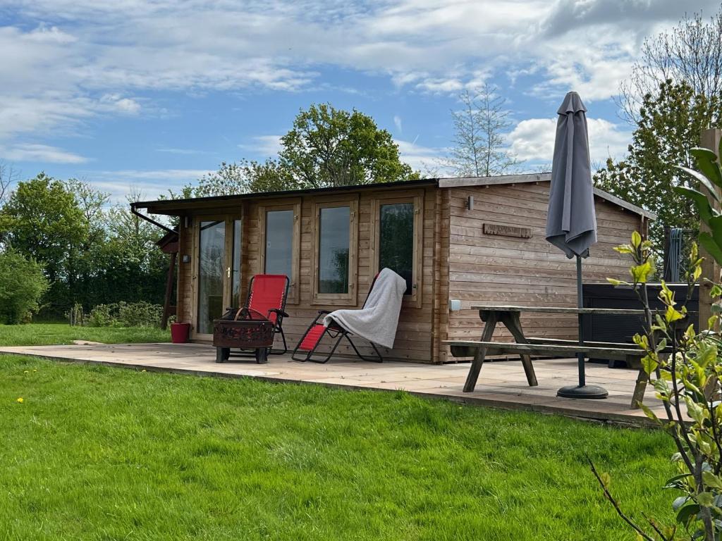 eine Hütte mit einem Tisch, 2 Stühlen und einem Sonnenschirm in der Unterkunft Silver Springs Farm Lodge in Dingestow